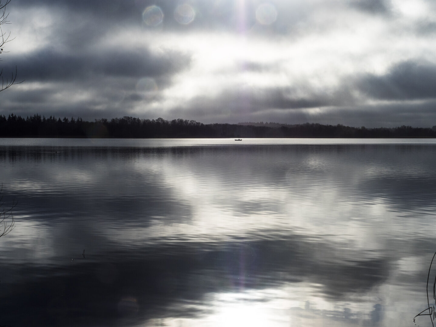 Noir et blanc. Sur un plan d'eau calme et sous un ciel nuageux, une toute petite barque au loin